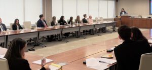 A group of associates in a conference room listening to a speaker at a podium.